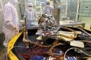 Three people wearing white Tyvek suits gather around a space instrument in a laboratory. 